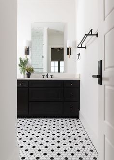 a bathroom with black and white tile flooring next to a large mirror on the wall