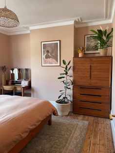 a bed room with a neatly made bed and a plant on the dresser next to it