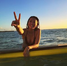 a woman in a bathing suit is sitting on a boat and making the peace sign