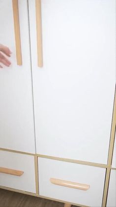 a person reaching for something on top of a white and wood cabinet with two handles