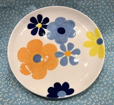 a white plate with blue, yellow and orange flowers on it sitting on a table