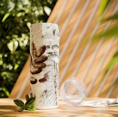 a white vase sitting on top of a wooden table next to a green leafy plant