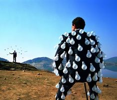 a man standing on top of a hill with lots of light bulbs attached to his back