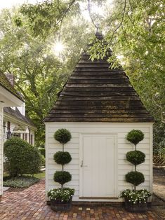 a small white house with potted plants on the front and side of it, surrounded by trees