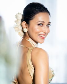 a woman with a flower in her hair smiling at the camera while wearing a gold dress