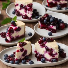 several slices of cheesecake with blueberries and mint on white plates sitting on a wooden table