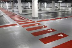 an empty parking garage with red arrows painted on the floor and white columns in the background