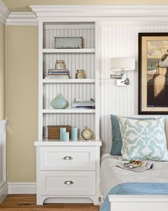 a bedroom with a white bookcase and blue pillows on it's side table