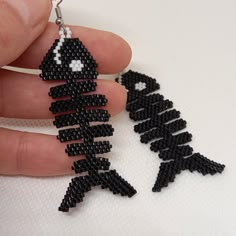 a hand holding a pair of black beaded earrings with an image of a skeleton on it