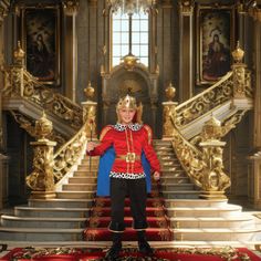 a man dressed in red and gold standing on stairs with his arms out to the side