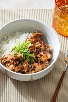 a white bowl filled with rice and meat on top of a place mat next to a fork