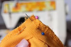 someone is stitching something with pins on the side of a yellow piece of fabric