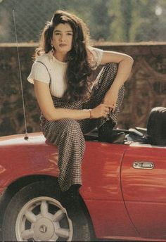 a woman sitting on the hood of a red car