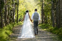 a bride and groom walking down a path in the woods holding hands with each other