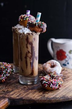 two glasses filled with ice cream and doughnuts on top of a wooden table