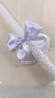 a white candle with a purple bow on it sitting next to a ribbon and pen