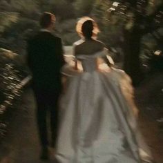 a man and woman in formal wear walking down a path