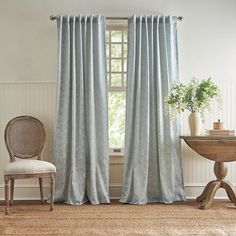 a chair and table in front of a window with drapes on it's sides