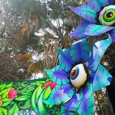 an elaborately decorated blue flower with green leaves in the foreground and trees in the background