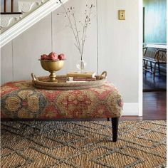 a bowl of fruit sitting on top of a footstool in front of a stair case