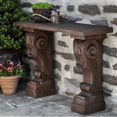 a wooden table sitting in front of a stone wall next to a potted plant