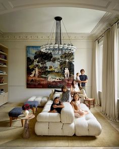 a group of people sitting on top of a white couch in a living room next to a painting