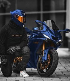 a man kneeling next to a blue motorcycle on a brick road in front of a building