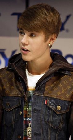 a young man wearing a denim jacket and gold earring is looking at the camera