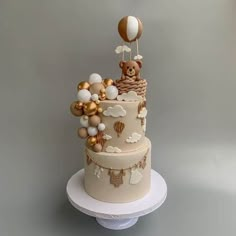 a three tiered cake decorated with balloons and a teddy bear in a basket on top