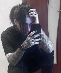 a man with black hair and tattoos is looking at his cell phone while sitting in front of a mirror