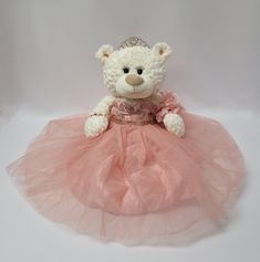 a white teddy bear wearing a pink dress with a tiara on it's head