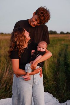 a young man and woman holding a baby in their arms while standing next to each other