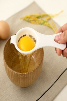 a person is pouring eggs into a small wooden bowl on a table with two eggs in the background