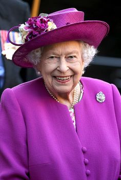 an older woman wearing a purple coat and hat with flowers on the side, smiling