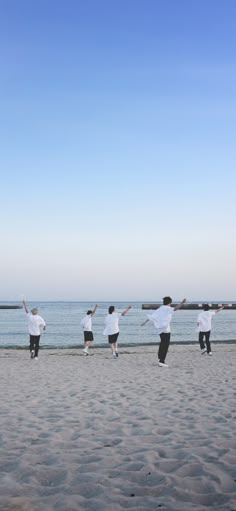 four people are running on the beach with their arms in the air and one person is flying a kite