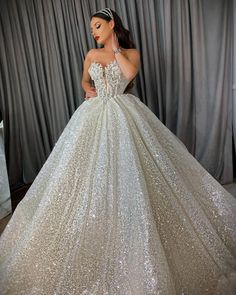 a woman in a white ball gown is standing next to a gray curtain and posing for the camera