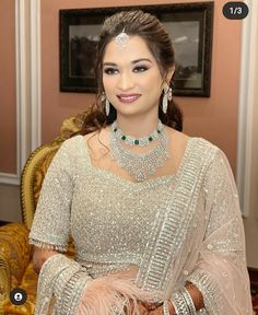 a woman in a white dress sitting on a couch wearing an elaborate necklace and earrings