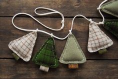 three small christmas trees hanging from strings on a wooden surface, with one being made out of fabric