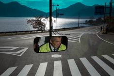 a man in a yellow jacket is looking out the side view mirror at water and mountains