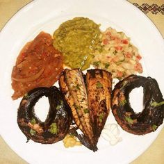 a white plate topped with grilled fish and veggies next to onion rings