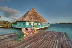 two chairs are sitting on a wooden dock next to a house with thatched roof