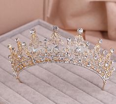 a gold tiara with crystal stones on it sitting on a white table next to a pillow