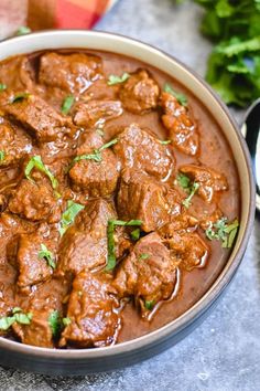 a bowl filled with meat and garnish next to some cilantro leaves