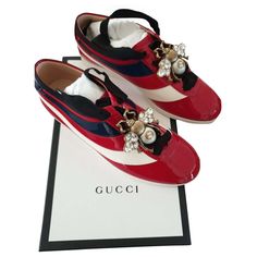 GUCCI Falacer Patent Leather Sneaker With Web In Red. the low-top sneaker is designed with a retro influence in patent leather with sylvie web stripe along the sides. each sneaker features a detachable crystal bee that can be attached using the front laces. the back heels are finished with bee embroidered metallic leather in contrasting colors-a distinctive house detail that began with the ace sneaker. hibiscus red patent leather black grosgrain trim patent leather sylvie web detachable metal bee appliqué with pearl and crystals red metallic leather detail on the back of one shoe and blue metallic leather detail on the back of the other shoe with gold embroidered bee rubber sole 0.5 height Size EUR 35 / US 5 Metal Bee, Crystals Red, Embroidered Bee, Mens Monogram, Hibiscus Red, Crystal Sunglasses, Gold Sneakers, Suede Ballet Flats, Gucci Sneakers