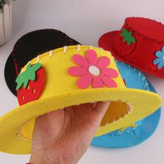 a hand is holding up three hats with strawberries and flowers on the top one