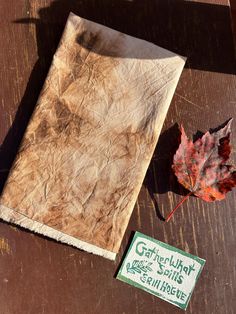 a leaf laying on top of a wooden table next to a paper bag and tag