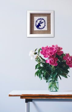 a vase with pink and white flowers on a table in front of a framed picture