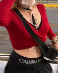 a woman wearing a red shirt and black shorts with tattoos on her stomach, holding a camera