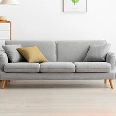 a grey couch sitting in front of a white wall next to a wooden table and lamp