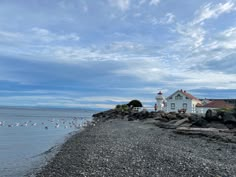 a white house sitting on top of a rocky beach next to the ocean with seagulls flying around